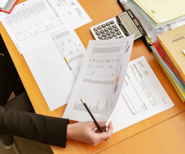 a brightly colored wooden desk with a person sitting at it taking notes with a few pieces of paper in front of them on the desk. they hold one of the papers and a pen in their right hand