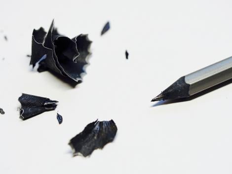 a sharpened black pencil with its pencil shavings next to it