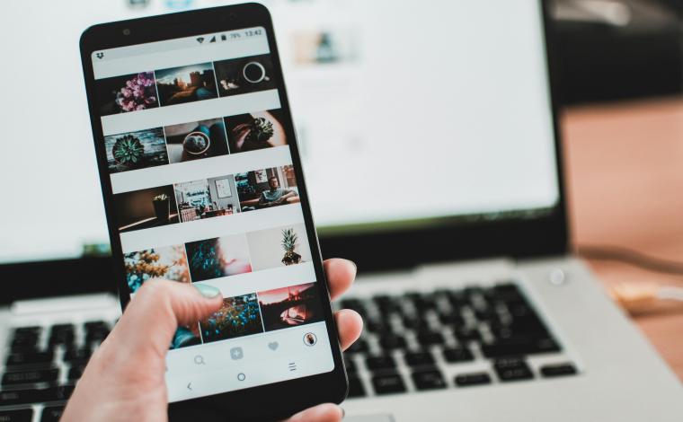 someone holds up a phone displaying photos on it, the phone is in front of an open laptop