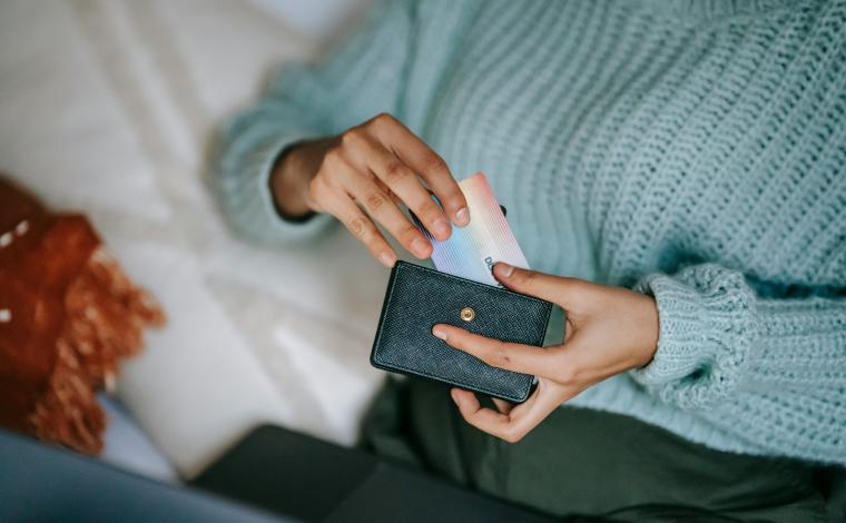 a person in a light blue sweater takes a rainbow colored credit card out of their wallet