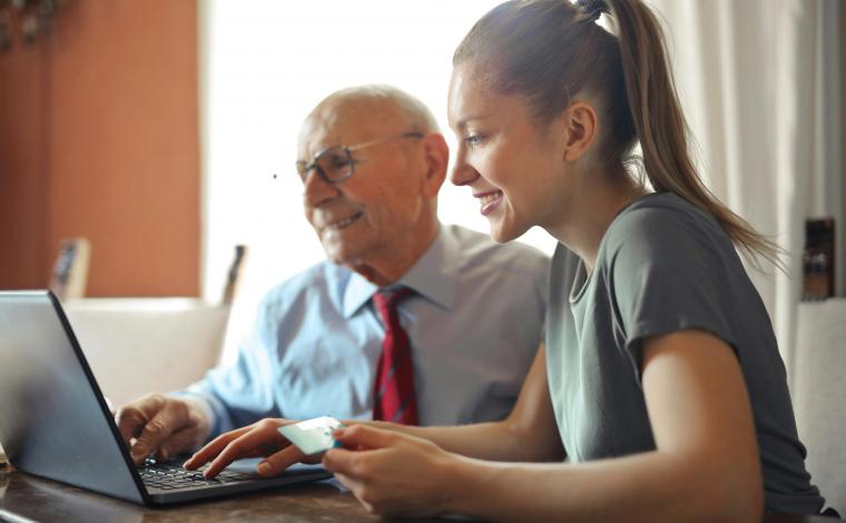 an older man in a suit and a younger woman both look happily at an open laptop