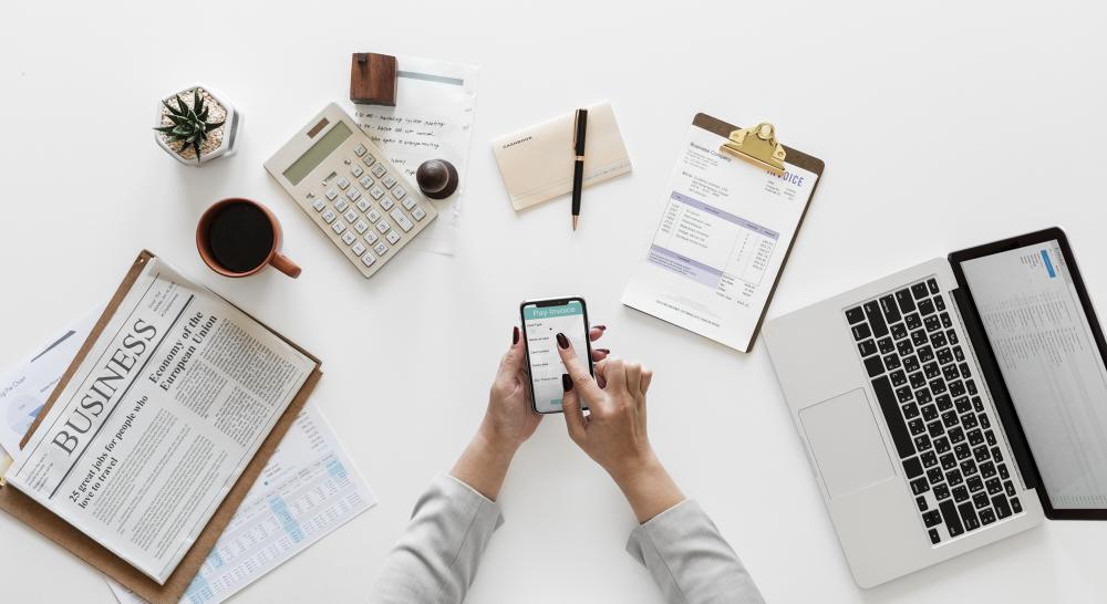 photo of a spread of office items on a desk such as a notebook, a mug, sticky notes, a notepad, and an open laptop