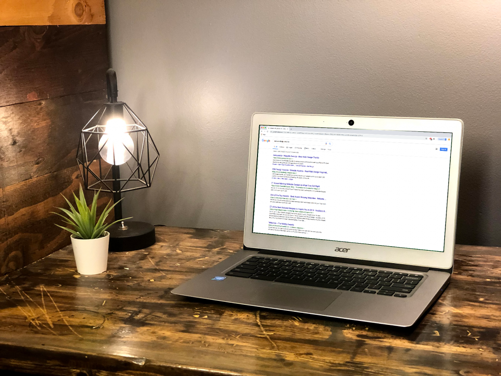 a laptop open on a wooden desk with a small plant and a light next to it