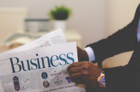 man holding a newspaper that has the word "business" as the title/headline