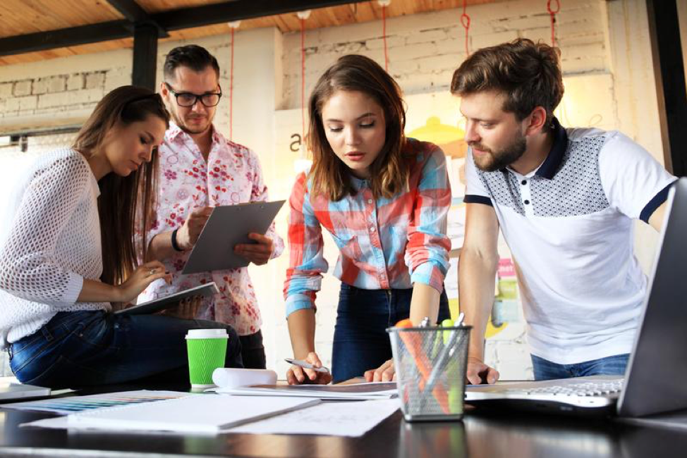 a group of 4 people are hunched over a desk with paper and office supplies on it