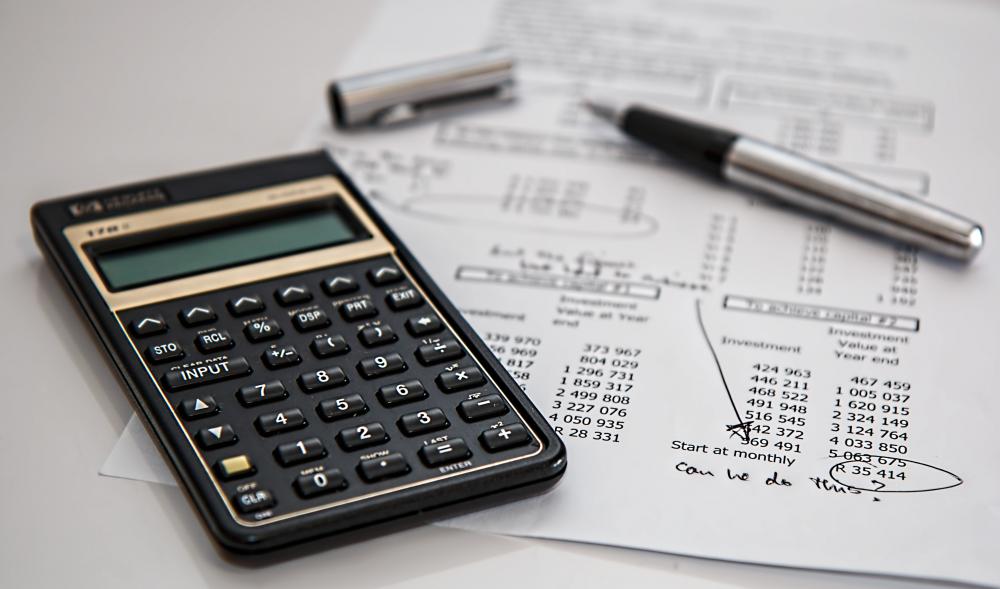 a calculator next to a paper with notes on it and a pen open with its pen cap beside it