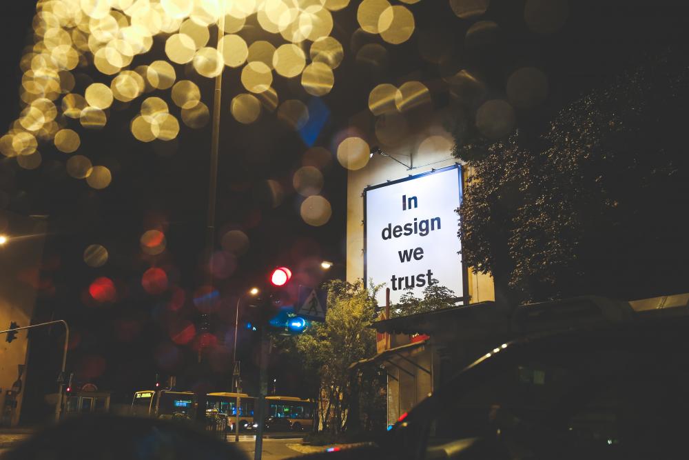 a lit billboard that says "in design we trust"