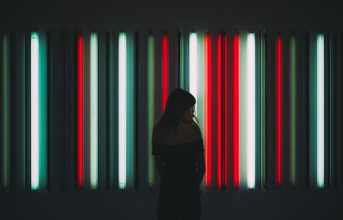 a girl standing in front of a plethora of long colored lights