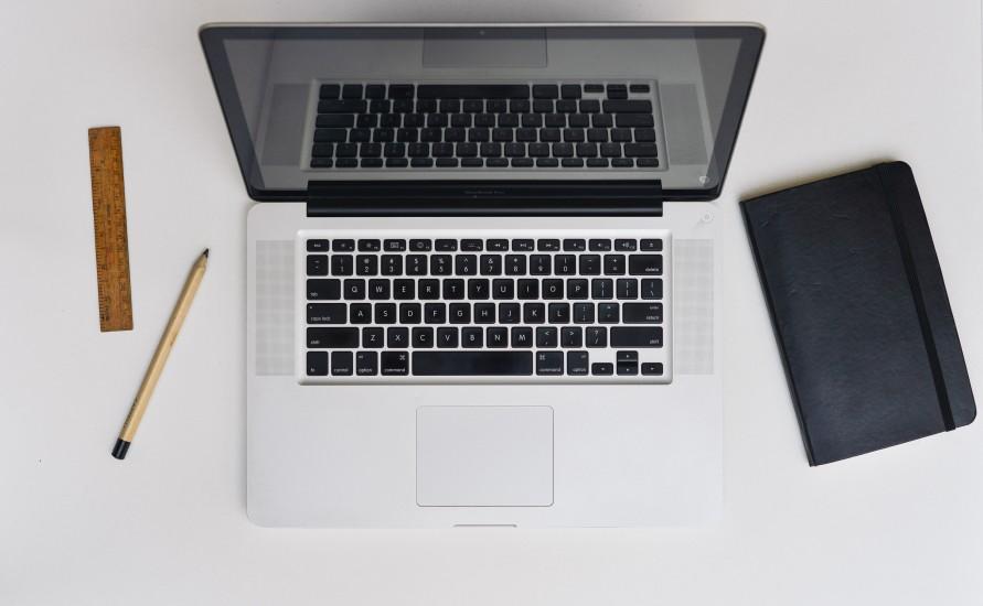 an open laptop with a black notebook to its right and a pencil and ruler to its left