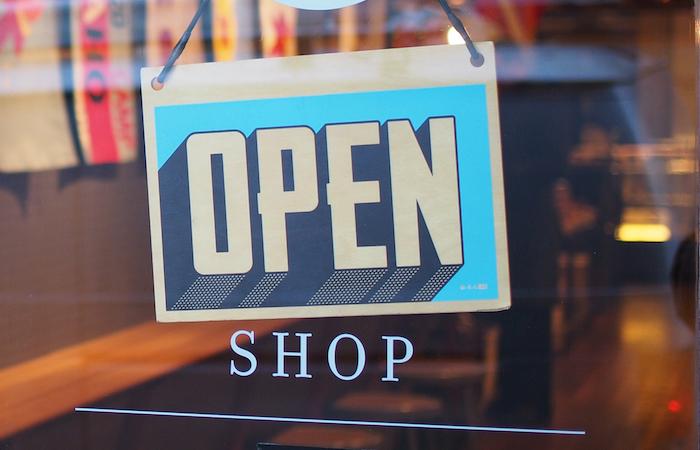 a blue "open" sign on a glass door. underneath the sign it says "shop" directly on the door in small capital letters