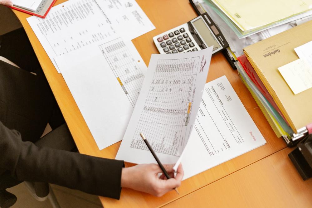 a brightly colored wooden desk with a person sitting at it taking notes with a few pieces of paper in front of them on the desk. they hold one of the papers and a pen in their right hand