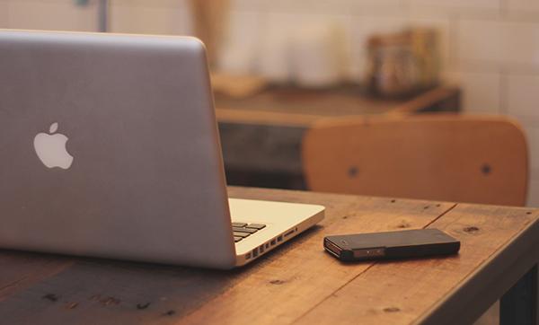 a black phone on a desk with a laptop next to it facing away from the viewer