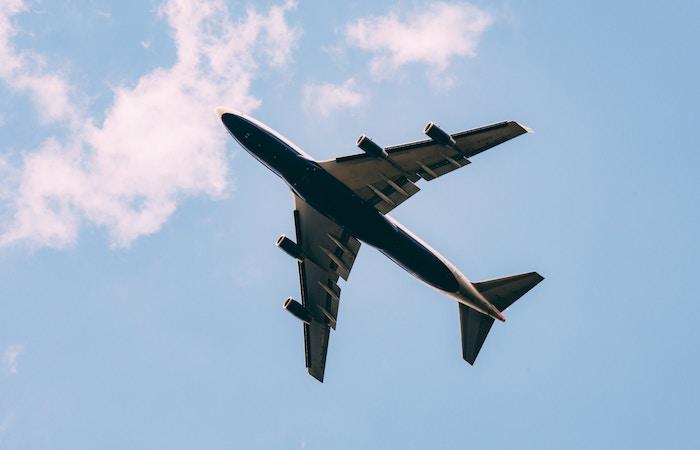 a plane's underside as it flies overhead. there are light clouds behind it and a pale blue sky