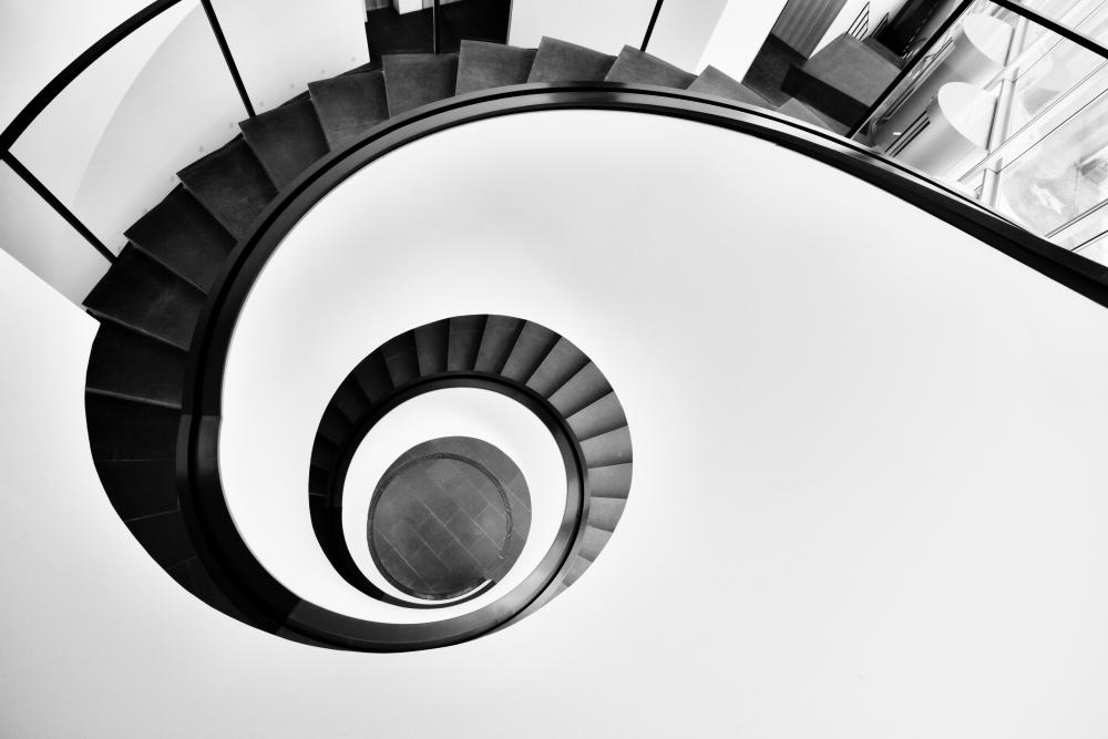 the top of a black spiral staircase contrasted to a white wall around it