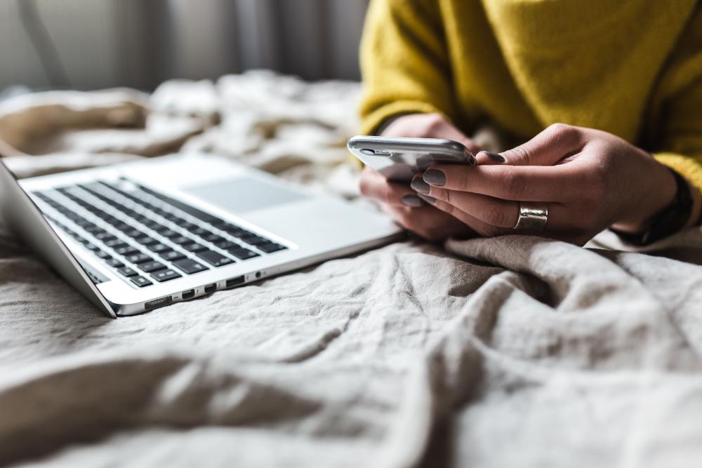 person looking at their phone next to an open laptop